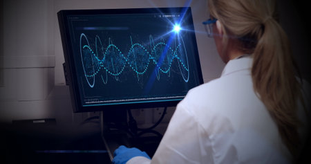 Caucasian scientist examining complex data on monitor. Wearing a white lab coat, blonde hair tied...