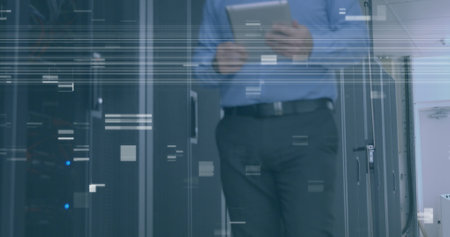 Caucasian middle-aged man holding tablet, walking in office. Wearing blue shirt and dark pants,...