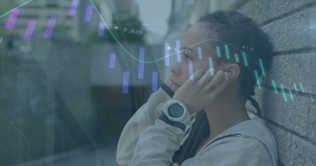 Image of graph, biracial woman taking wall support and listening to music using headphones. Changing numbers, digital composite, report, business, growth and technology concept.の写真素材