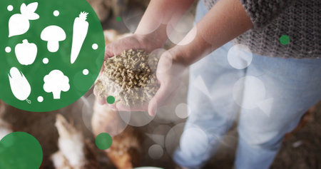 Image of vegetable icons and spots over mid section of woman feeding chickens in poultry farm. Livestock breeding conceptの写真素材