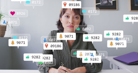 Image of social media icons over focused asian woman talking looking at the camera at office. Social...