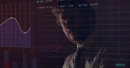 Caucasian young man analyzing financial graphs on transparent screen. Office environment with...