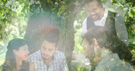 Image of lights over happy diverse friends having picnic with wine on sunny day. wine business, party, celebration and spending time with friends concept digitally generated image.の写真素材