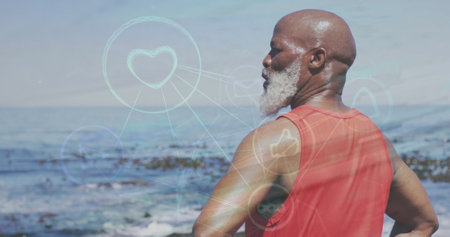 Image of network of digital icons over african american senior man standing near the sea. Sports and fitness technology conceptの写真素材