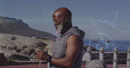 Image of african american middle-aged man interacting with smartphone outdoors. he is standing near a rocky coastline with digital graphics overlaying sceneの写真素材