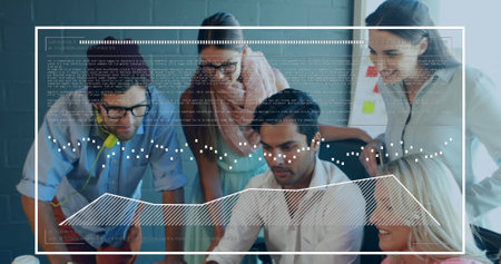 A diverse group of young and middle-aged colleagues is collaborating on project using a computer. They are in a modern office with charts and data displayed on screenの写真素材