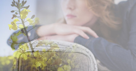 Image of flowers over caucasian woman sitting on sofa. Lifestyle and domestic life concept digitally...