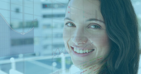 Image of financial graphs over happy caucasian female consultant working in office. global business, finance, economy and technology concept digitally generated image.の写真素材