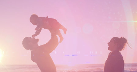 Image of light spots over happy caucasian couple with baby at beach. fathers day and celebration...