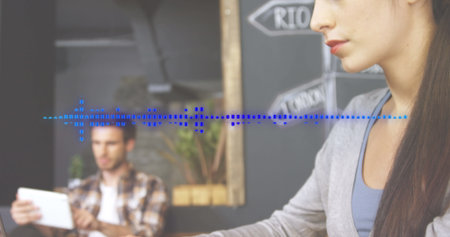 Image of soundwave over beautiful caucasian woman working on laptop in office. Digital composite,...