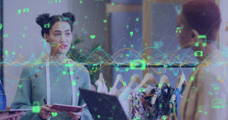 Image of graphs and connected icons over diverse female designers discussing about fashion. Digital composite, multiple exposure, report, business, communication and technology concept.の写真素材