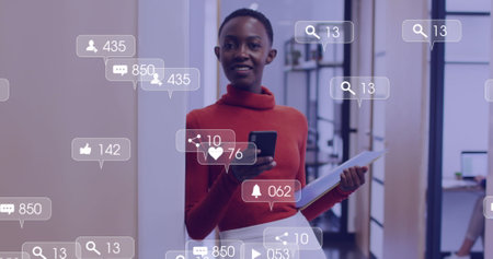 Image of media icons over happy african american businesswoman using smartphone. social media and...