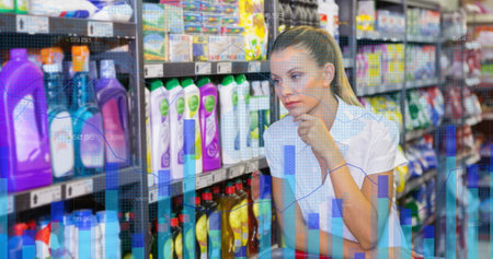 Caucasian woman thoughtfully looking at products on supermarket shelf. Graphs and data overlays suggest analysis or decision-making in a retail environmentの写真素材