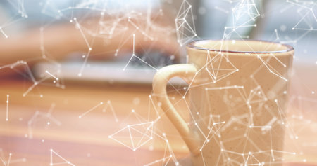 Person typing on laptop with coffee mug in foreground, digital network overlay visible. Wooden table and blurred background create cozy workspace atmosphere, enhancing focusの写真素材