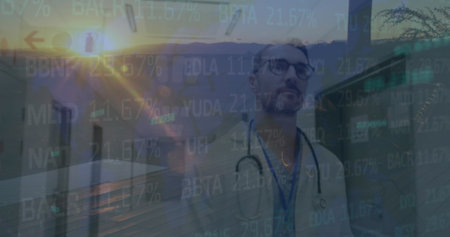 Image of caucasian male in his 40s wearing stethoscope, looking at a screen with data projections. sunset view and medical facility visible in backgroundの写真素材