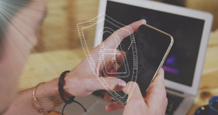 Young Caucasian person interacting with smartphone, showing screen with security icon. Wooden table and laptop in background suggest tech-focused environmentの写真素材