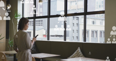 Image of multiple profile icons floating against asian woman using smartphone at office. Global...