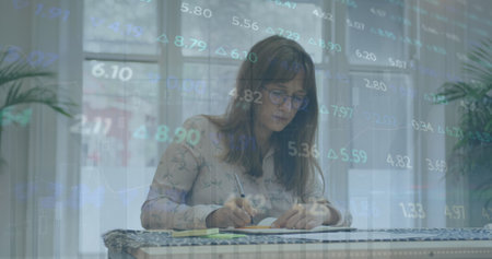 Image of stock market data processing against thoughtful caucasian woman taking notes at office. Global economy and business technology conceptの写真素材