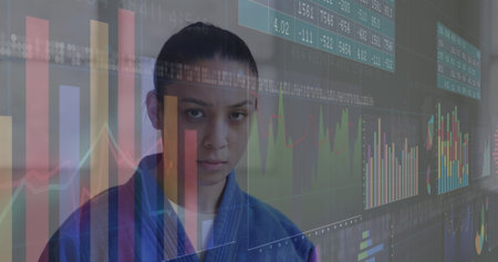 Image of graphs and number charts, serious biracial martial female artist standing against wall. Digital composite, multiple exposure, report, business, digits, karate, sports and competition.の写真素材