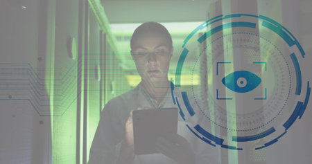 Image of eye over caucasian female engineer walking and using digital tablet in server room. Digital composite, multiple exposure, surveillance, business, networking and technology concept.の写真素材