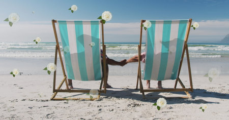 Image of white flowers over diverse couple in deckchairs holding hands on beach. holiday, love and leisure time concept digitally generated image.の写真素材