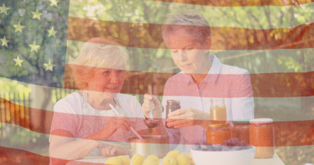 Image of flag of usa over senior caucasian female friends eating dinner outdoors. patriotism and celebration concept digitally generated image.の写真素材