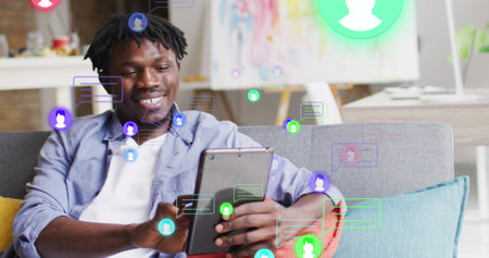 Image of media icons over happy african american man using tablet. Social media and digital interface concept digitally generated image.の写真素材