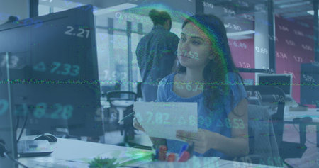 Image of stock market data processing against caucasian woman using computer at office. Global economy and business technology conceptの写真素材