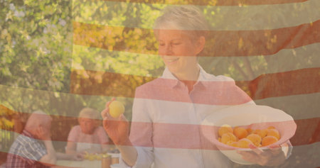 Image of flag of usa over senior caucasian friends eating dinner outdoors. patriotism and...