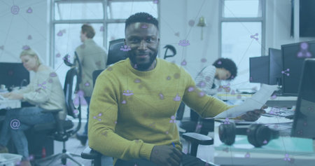 Image of network of digital icons over happy african american man holding document at office. Global networking and business technology conceptの写真素材