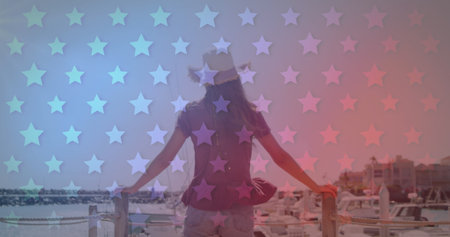 Independence text and multiple stars against rear view of woman standing on a wooden pier. american independence and celebration conceptの写真素材