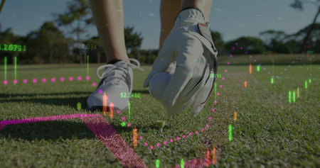 Image of graphs and numbers over low section of caucasian woman placing golf ball on tee. Digital composite, golf course, leg, shoe, hand, green, glove, sport, grass, hobby and competition.の写真素材