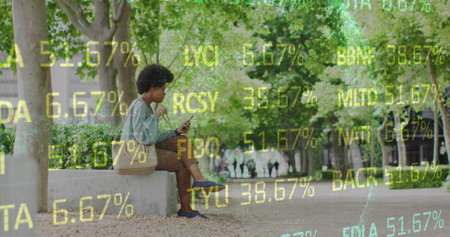Image of african american woman sitting in park and eating food while using on cellphone. Trading...