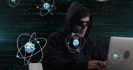 Image of atom structures over biracial male hacker using laptop to hack system. Digital composite, multiple exposure, cybercrime, particles, three dimensional , science and technology concept.の写真素材