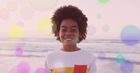 Smiling boy standing on beach with colorful bubbles in background. Childhood, happiness, outdoor, fun, summer, playfulの写真素材