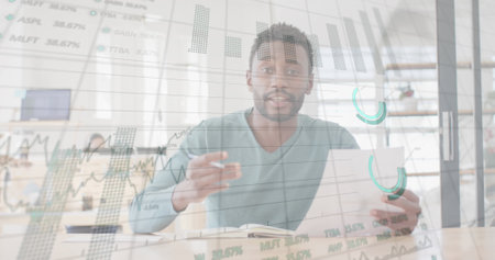 Image of graphs, trading board, biracial man writing in notepad, talking while looking at camera. Digital composite, multiple exposure, report, business, stock market and technology concept.の写真素材