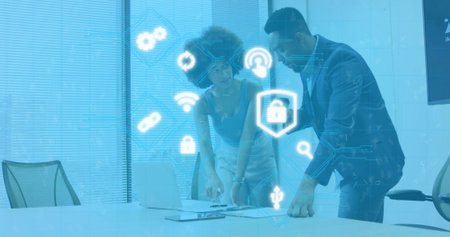 Image of illuminated icons over diverse coworkers discussing reports on laptop at office. Digital...
