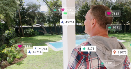 Caucasian grandfather looking at floating social media icons in garden. He has short grey hair,...