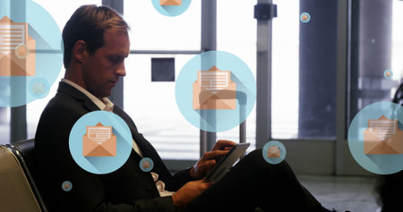 Image of message icons floating over caucasian businessman using digital tablet at an airport. Global networking and business technology conceptの写真素材