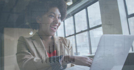 Image of changing numbers on graph over happy biracial woman scrolling on laptop. Digital composite, multiple exposure, report, business, growth and technology concept.の写真素材