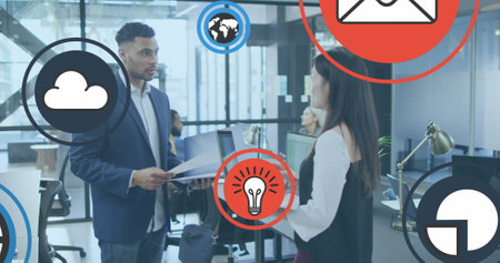 Image of multiple icons over diverse coworkers standing and discussing reports in office. Digital...