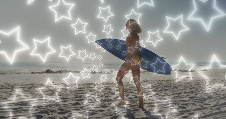 Image of neon stars over caucasian woman walking on beach with surfingboard. holidays, vacations and friendship concept digitally generated image.の写真素材