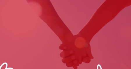 Two people holding hands against pink background. Sunlight casting warm glows and shadows over their handsの写真素材