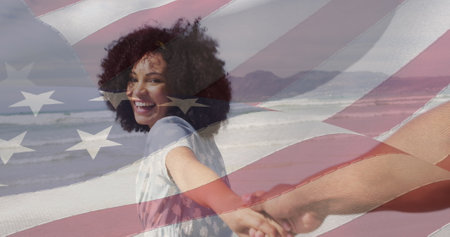 Image of flag of usa over happy african american couple on beach. American patriotism, nationality, summer and diversity concept digitally generated image.の写真素材