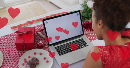 Image of heart icons over african american woman using laptop with copy space, slow motion. Valentine's day and love concept digitally generated image.の写真素材