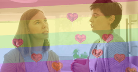 Image of heart emojis and rainbow flag over caucasian female couple at home. Lgbtq, love, romance and celebration concept digitally generated image.の写真素材