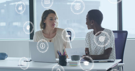 Image of digital icons over diverse business women in office. Global business, finances, computing...