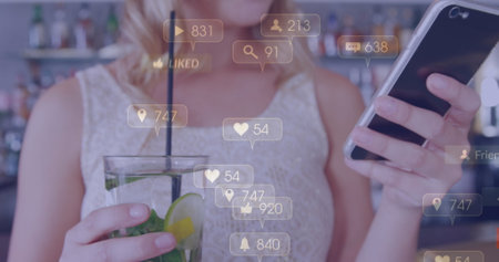 Image of media icons over caucasian woman with drink using smartphone. Social media and digital interface concept digitally generated image.の写真素材