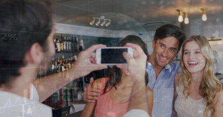 Image of data processing over caucasian male waiter taking picture of group of friends at a bar. Global finance and business technology conceptの写真素材