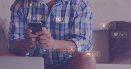 Image of media icons over african american man using smartphone. Social media and digital interface concept digitally generated image.の写真素材